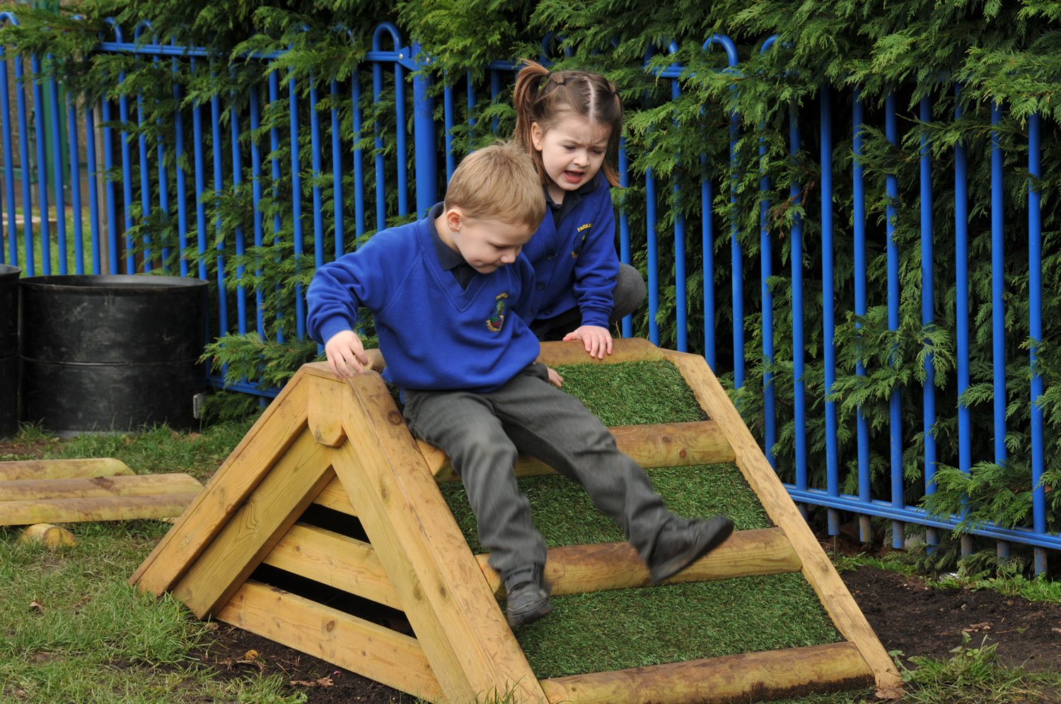 Two children in Parkside School uniform play on a wooden climbing structure in the playground. 
