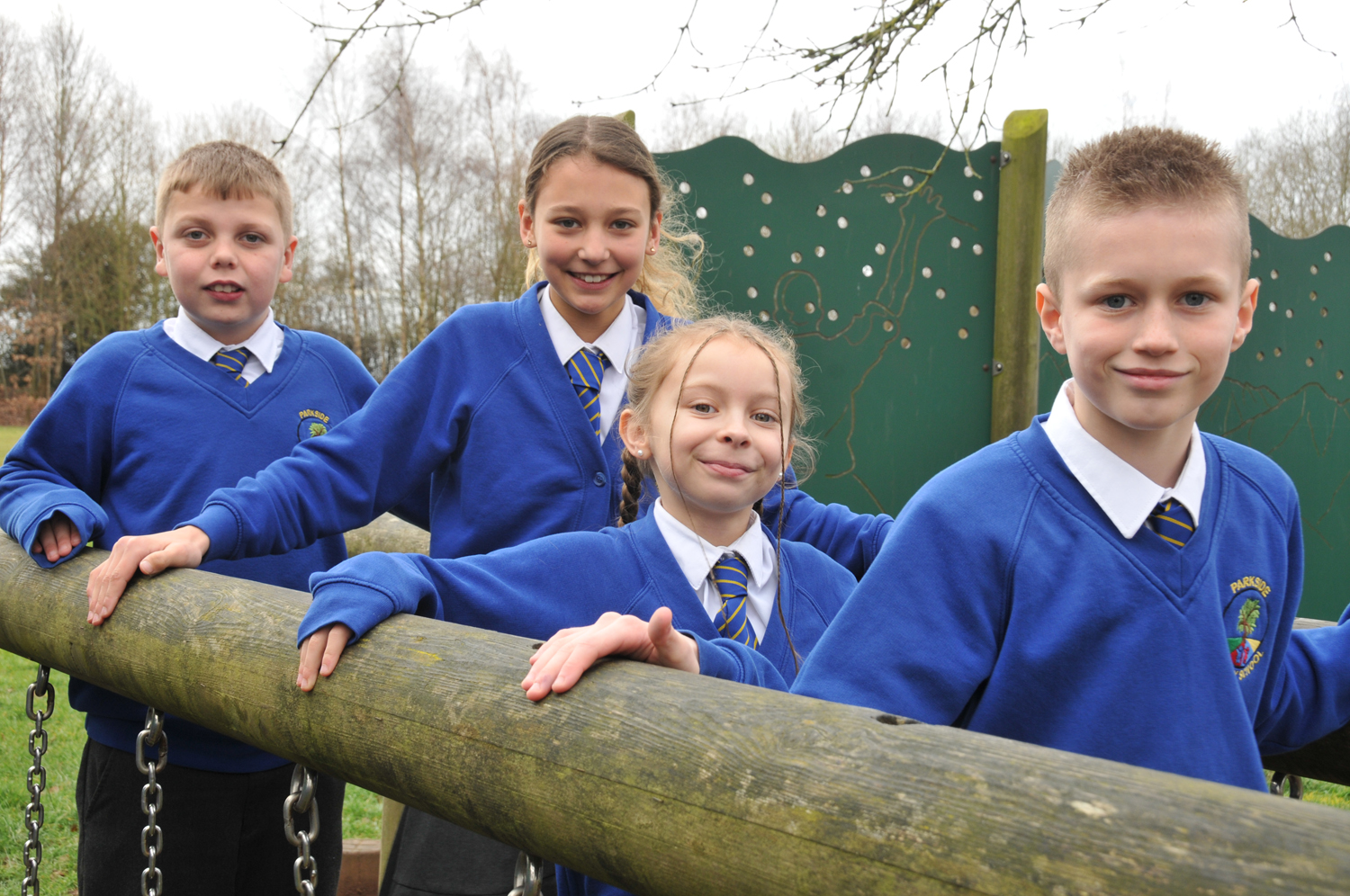 Smiling children in Parkside Primary School uniforms pose for a photo on a wooden play structure in one of our outside play areas.